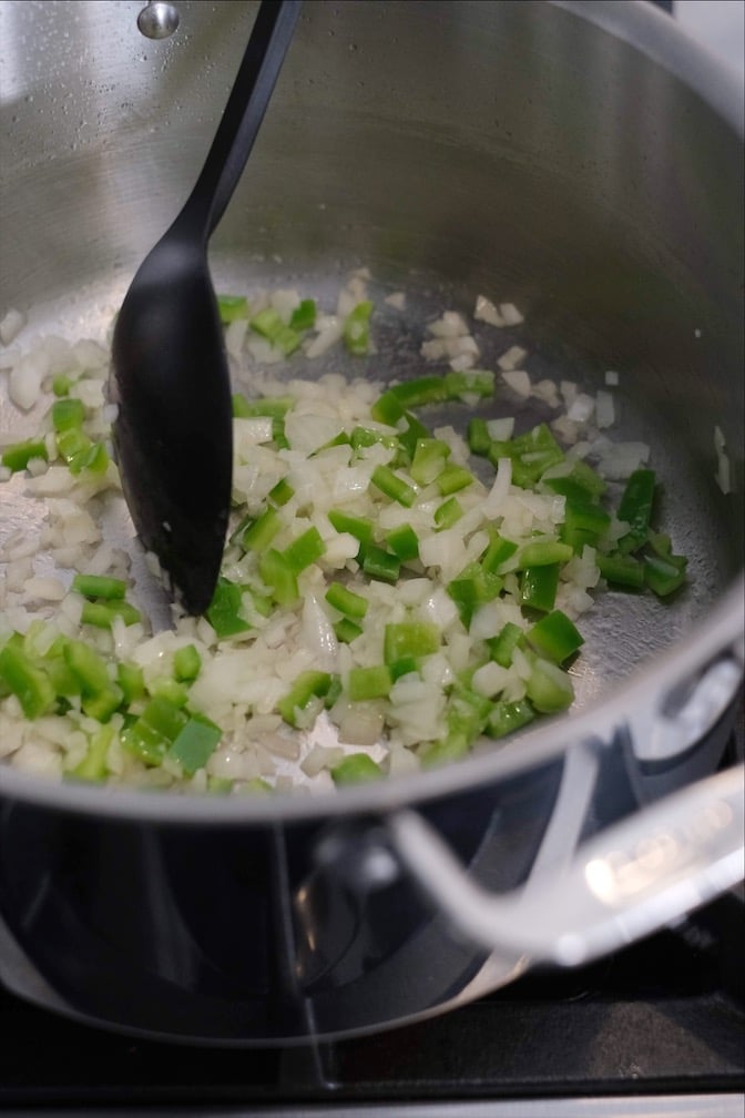 Chopped green bell peppers and chopped sauteing in a large pot. 