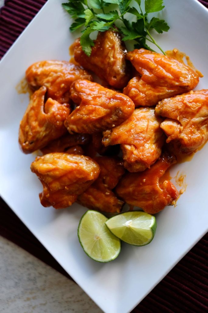 Baked buffalo chicken wings on a white platter with two lime wedges and parsley sprigs