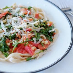 Brown rice pasta with arugula tomatoes sitting on a whit plate with black rim