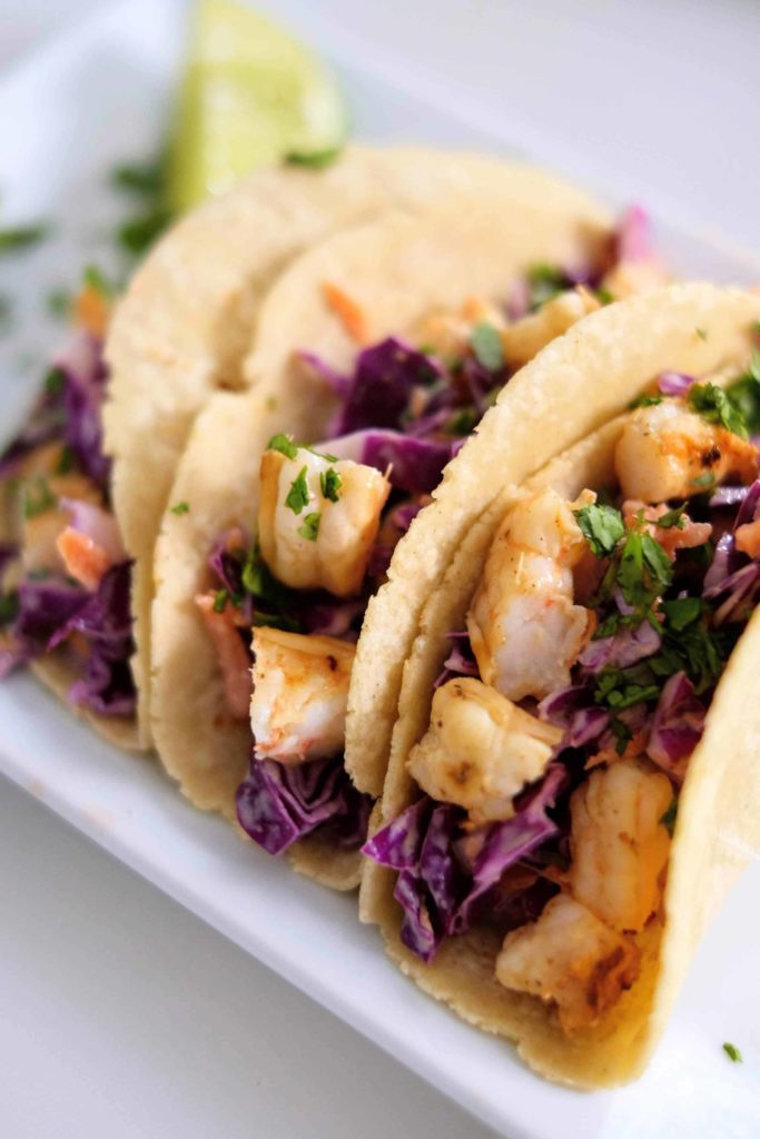 Three shrimp tacos sitting on a white platter.