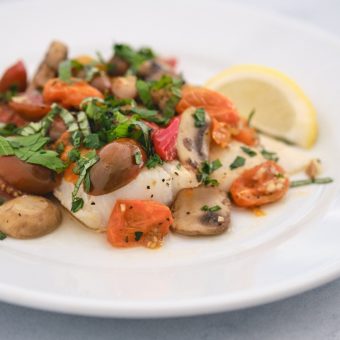Baked cod with tomatoes and mushrooms on a white plate