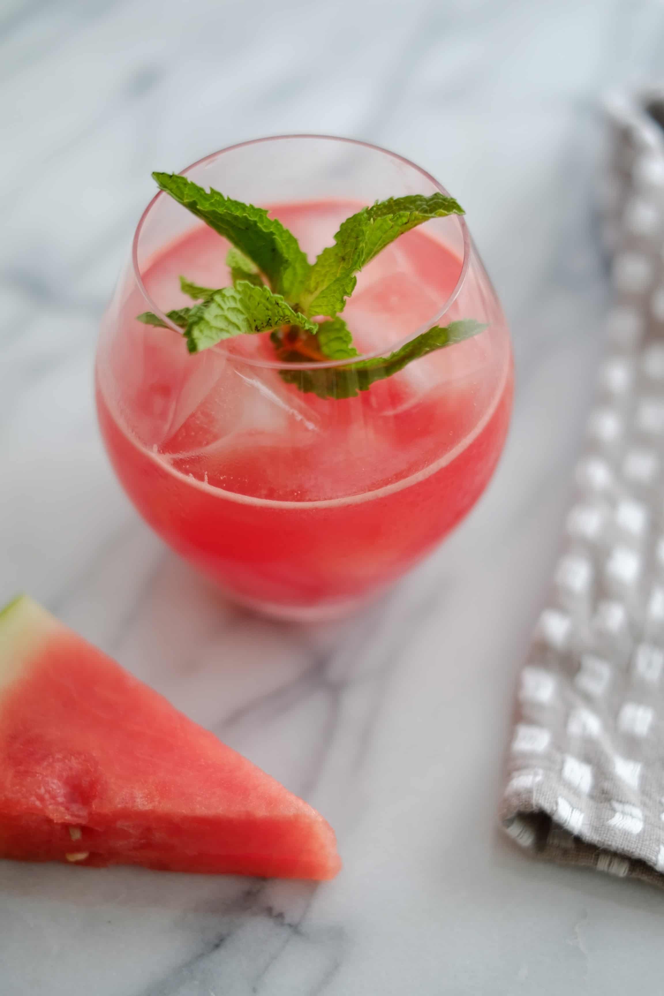 watermelon cocktail in a glass with mint on a marble counter with a wedge of watermelon