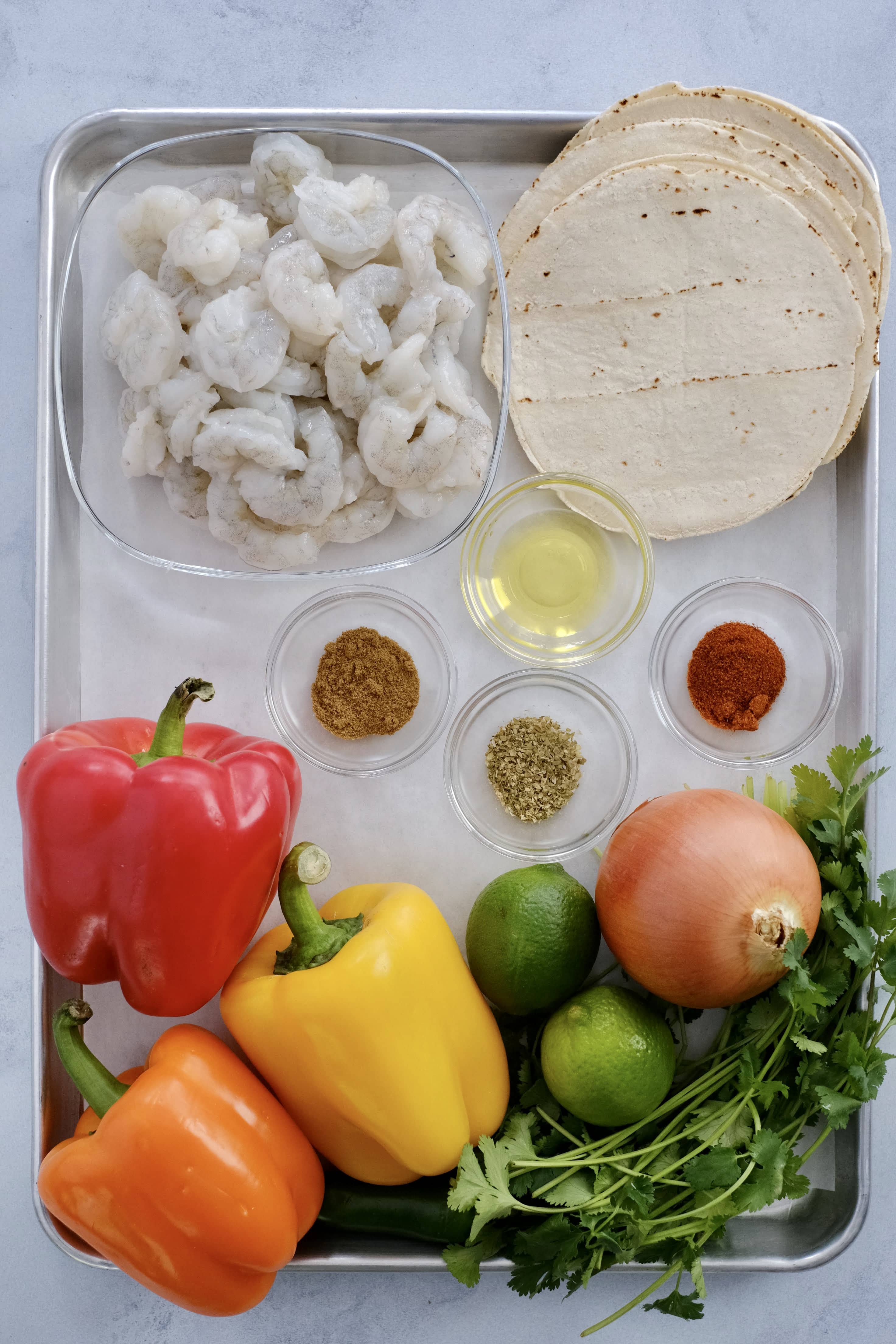 a sheet pan of raw shrimp tortilla bell peppers limes onions cilantro