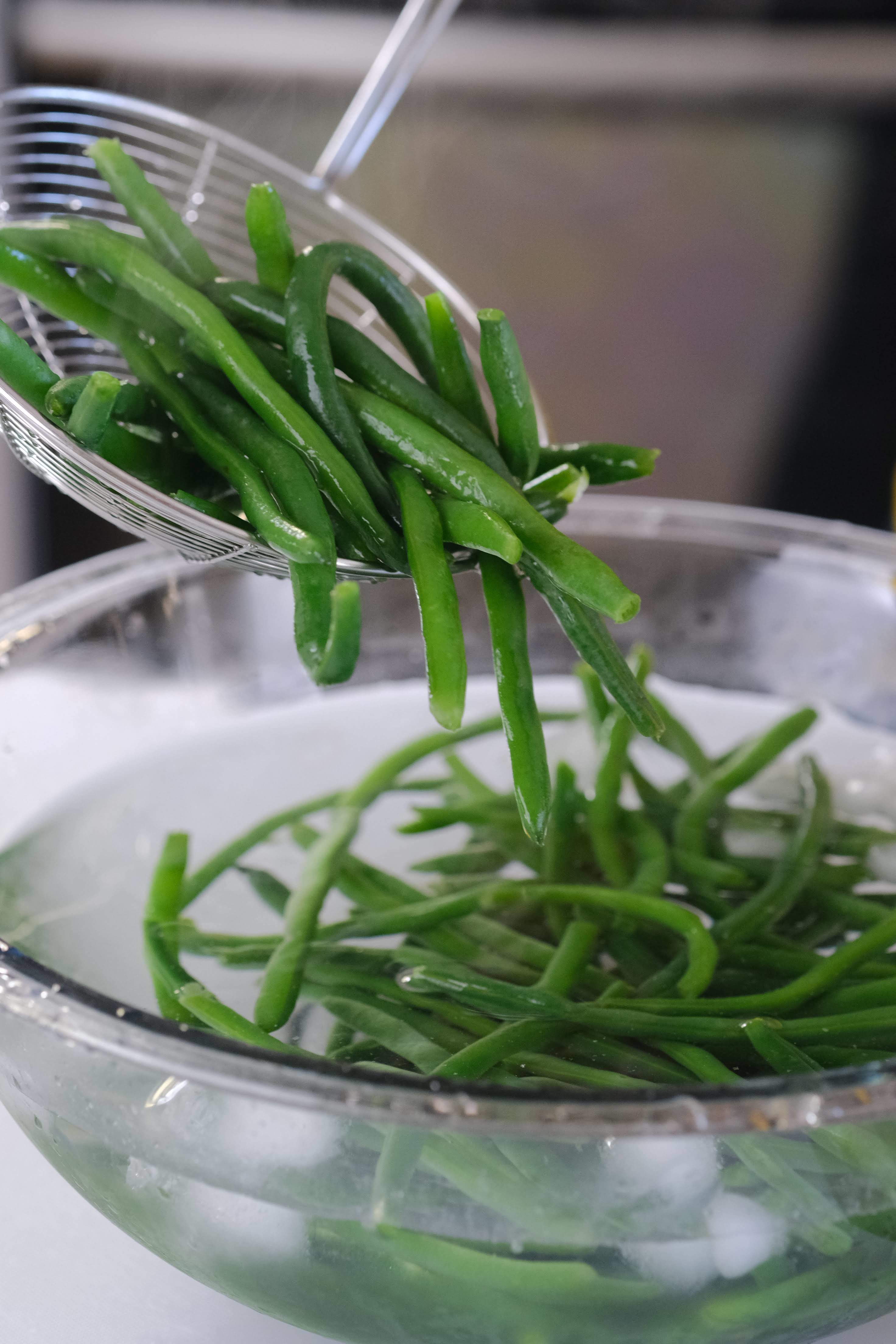 green beans in a clear bowl filled with ice water