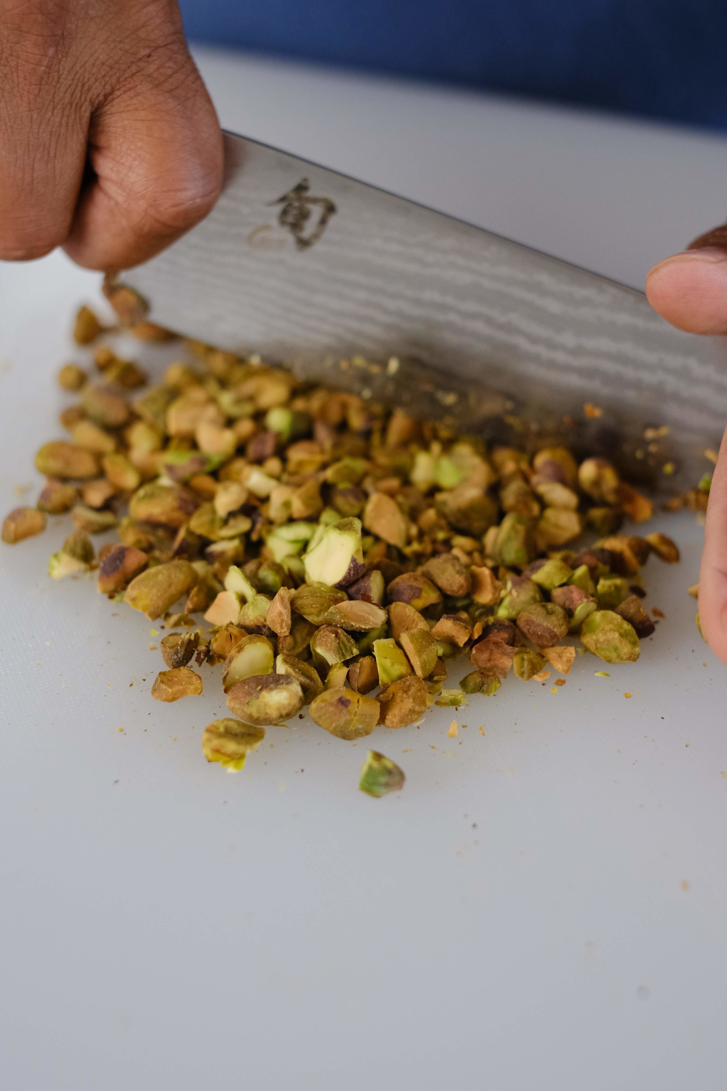 toasted pistachios being chopped with a knife on a white cutting board