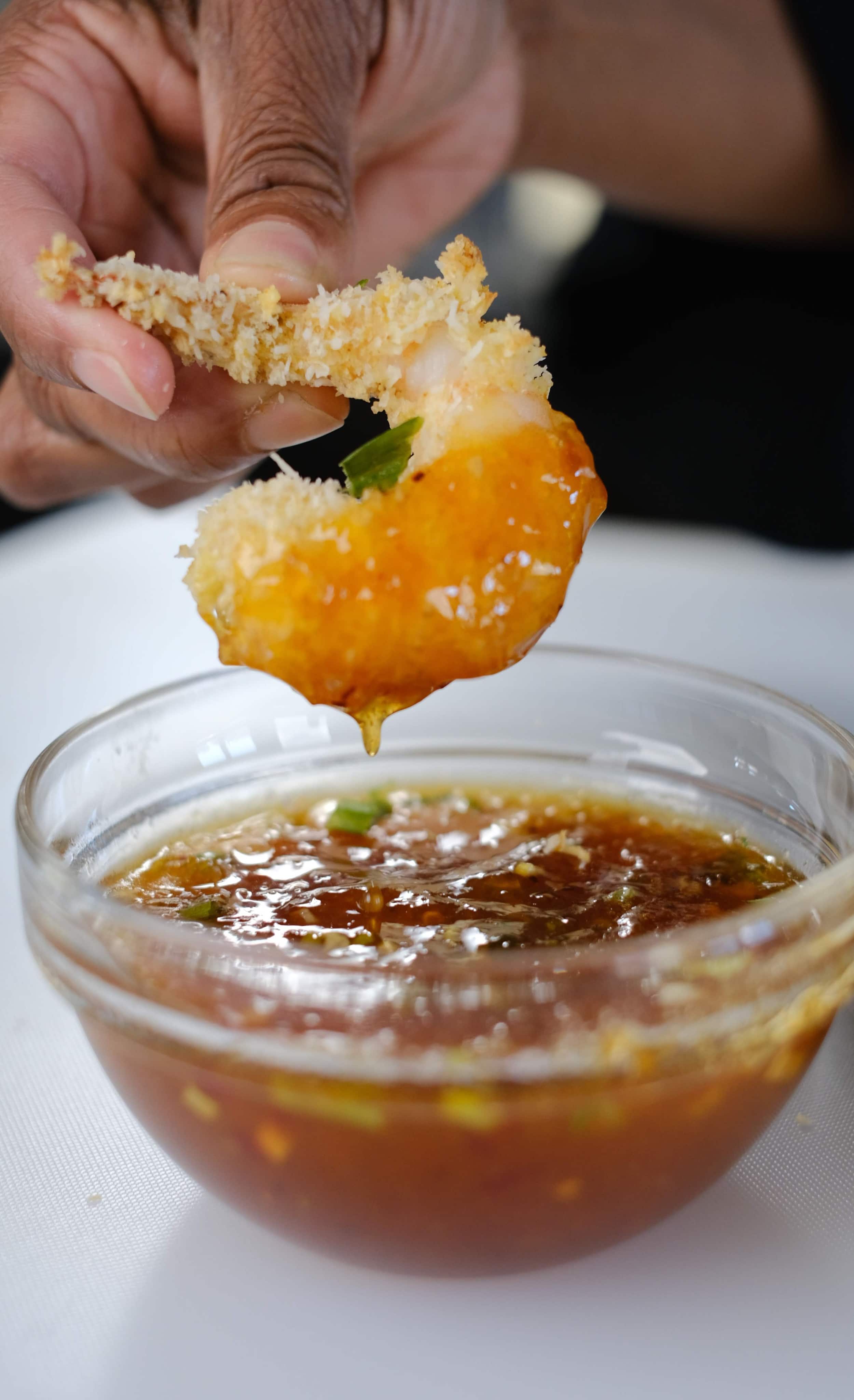 coconut shrimp being dipped in chili sauce